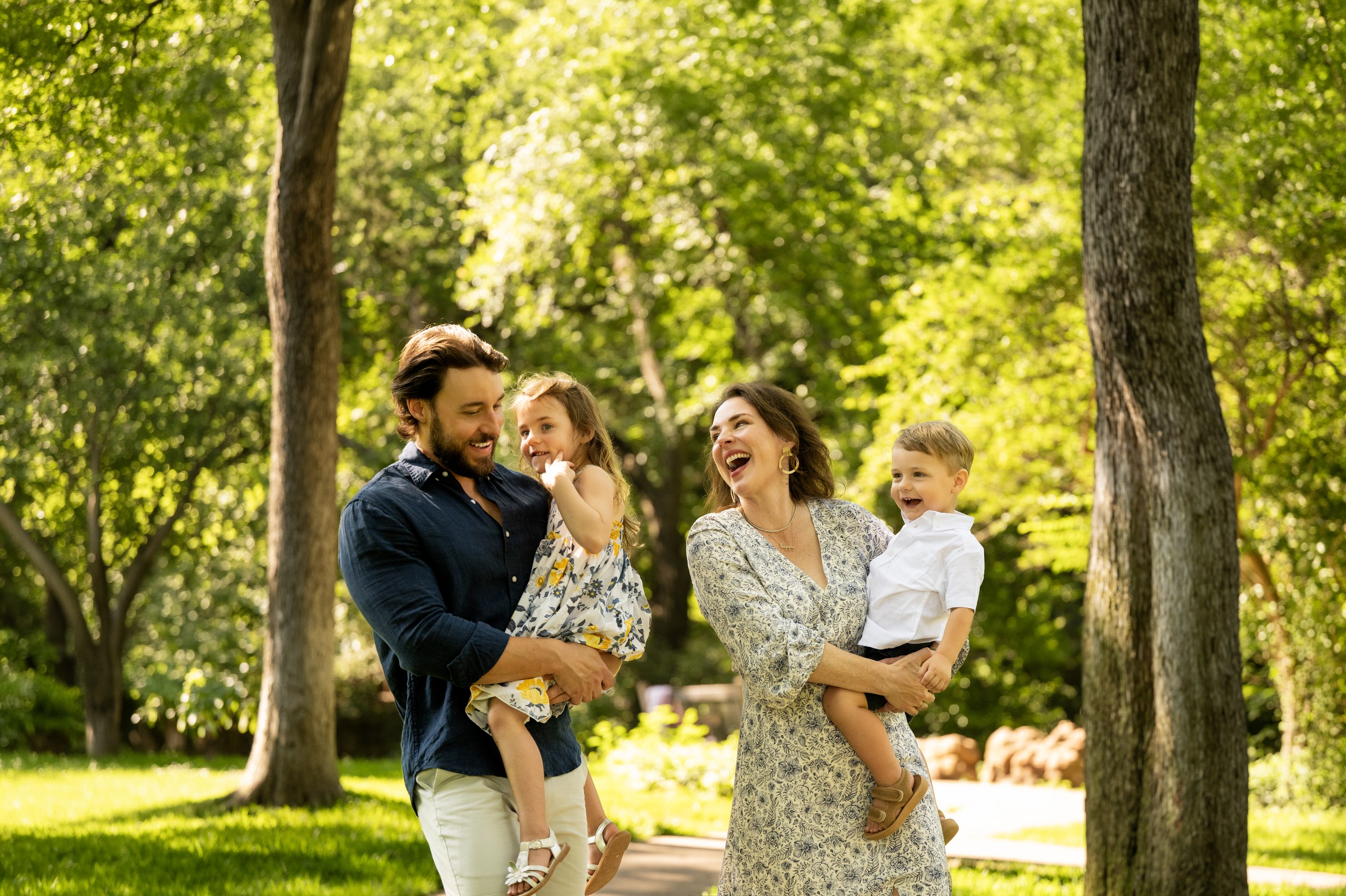 A Dallas family of four laughing together under the trees during a documentary family photography session