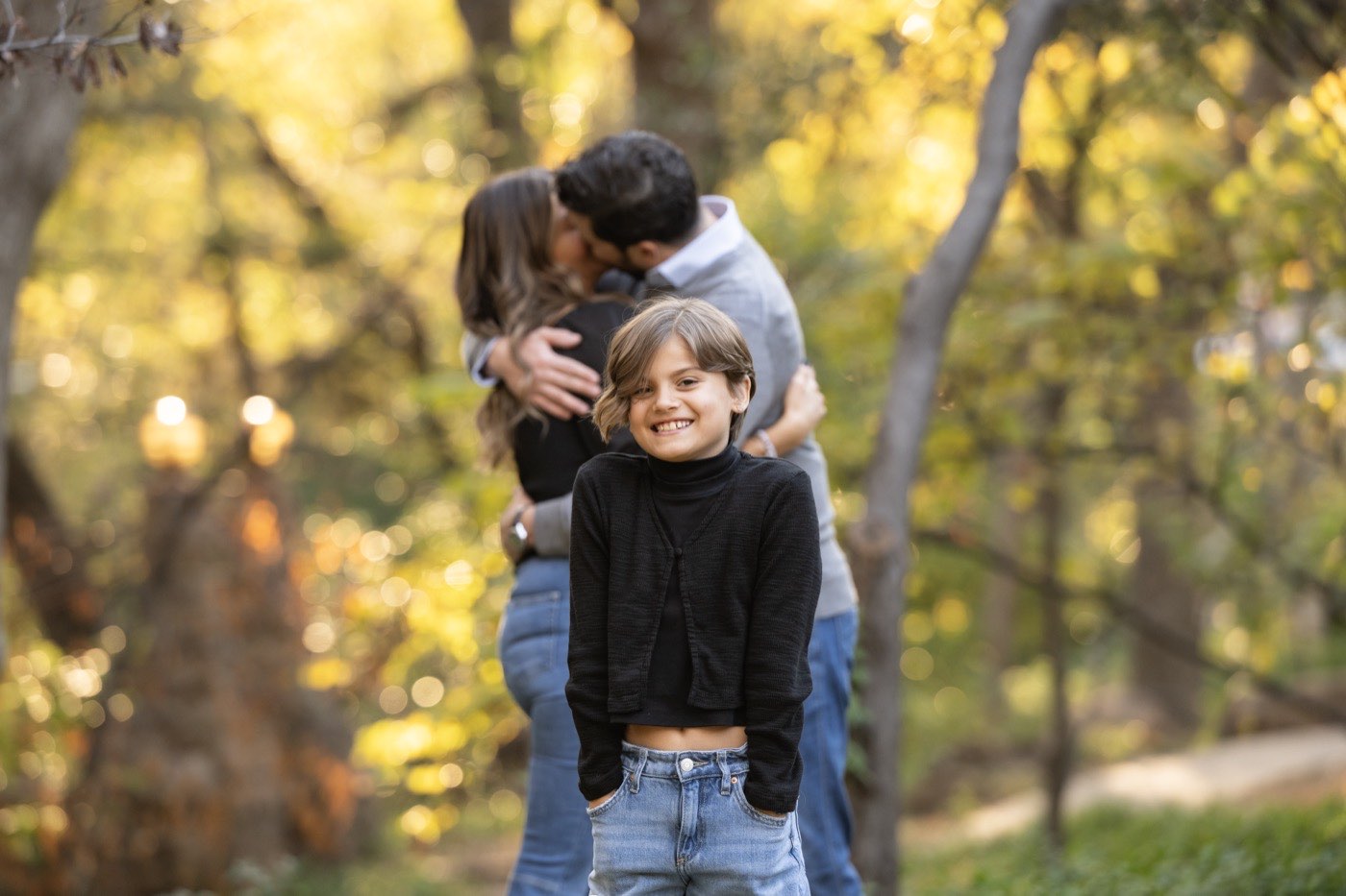 A young girl smiling while her parents embrace behind her during a fall family session in Dallas