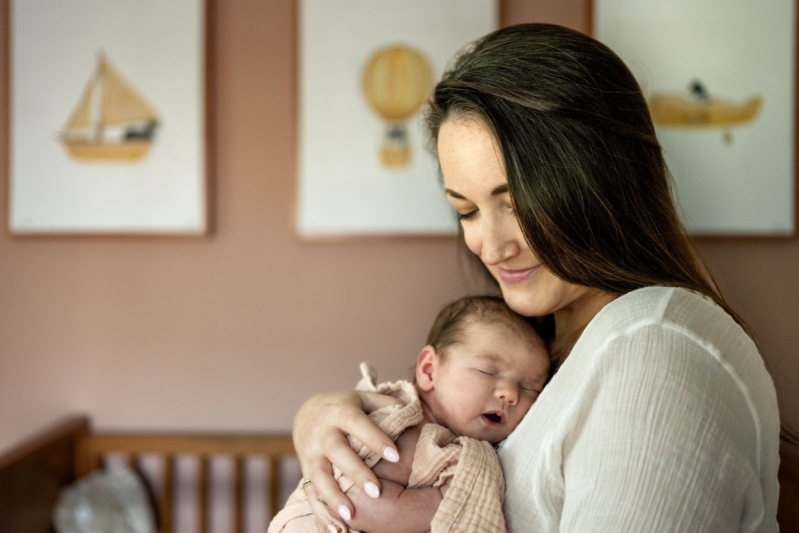 A mother holding her sleeping newborn in the nursery during an in-home newborn session in Dallas
