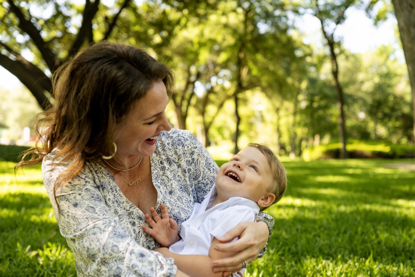 A Dallas mother laughing with her young son during an outdoor family portrait session